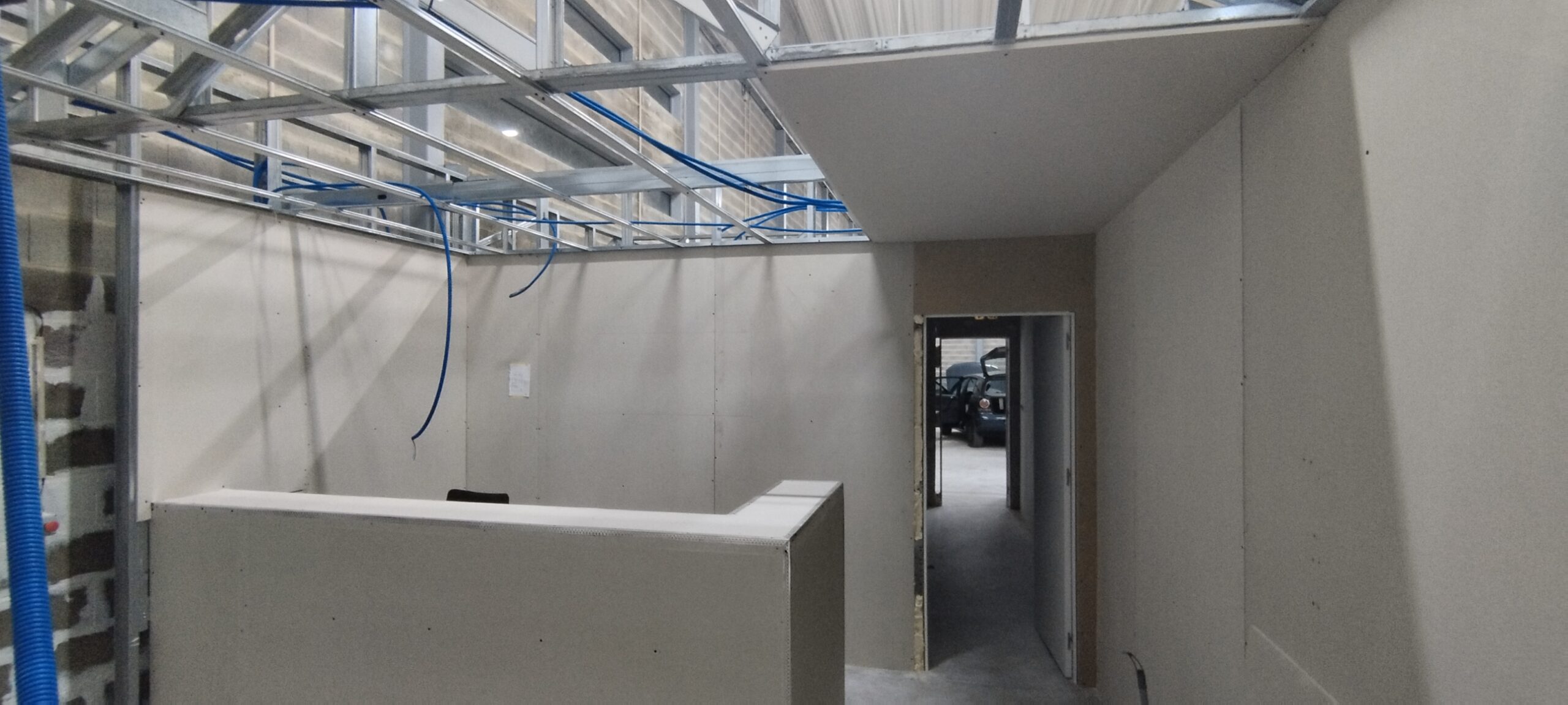 Divisórias e teto em placas de gesso durante a montagem, com perfis metálicos e instalações visíveis