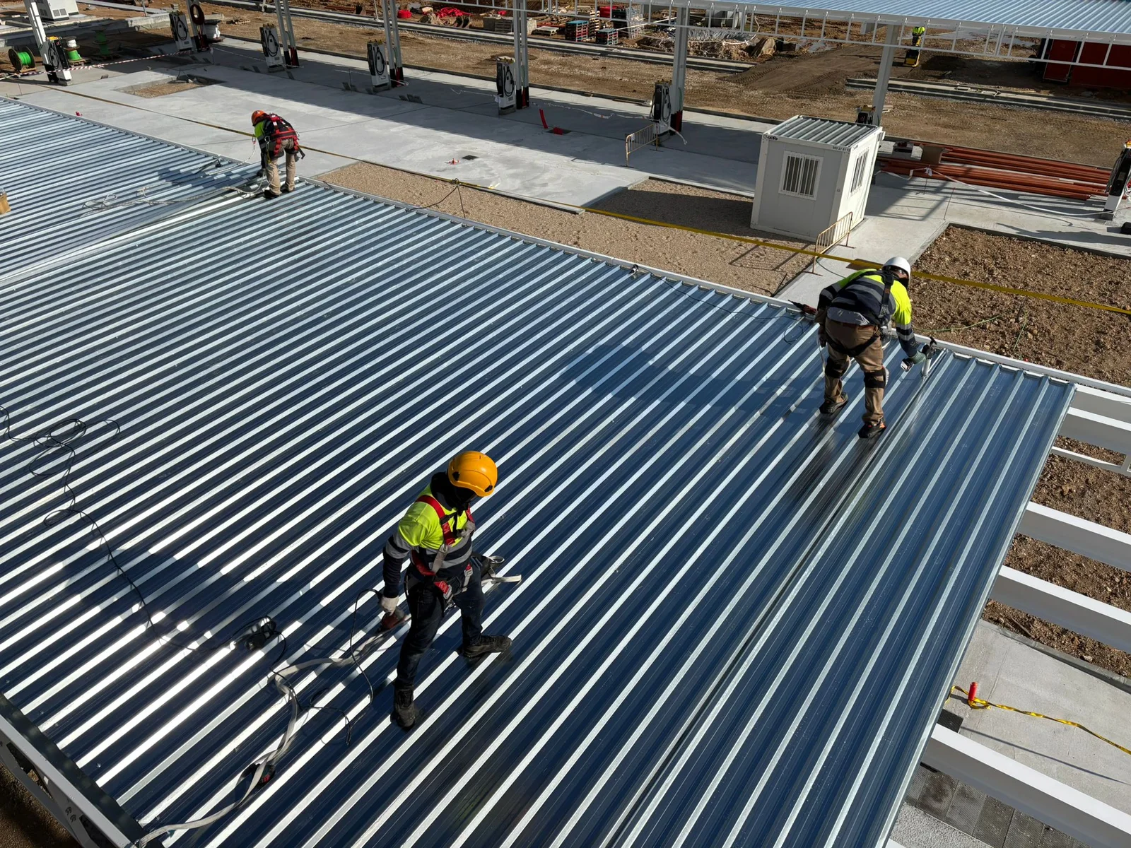 Equipa com capacetes e arneses durante a montagem de uma cobertura metálica
