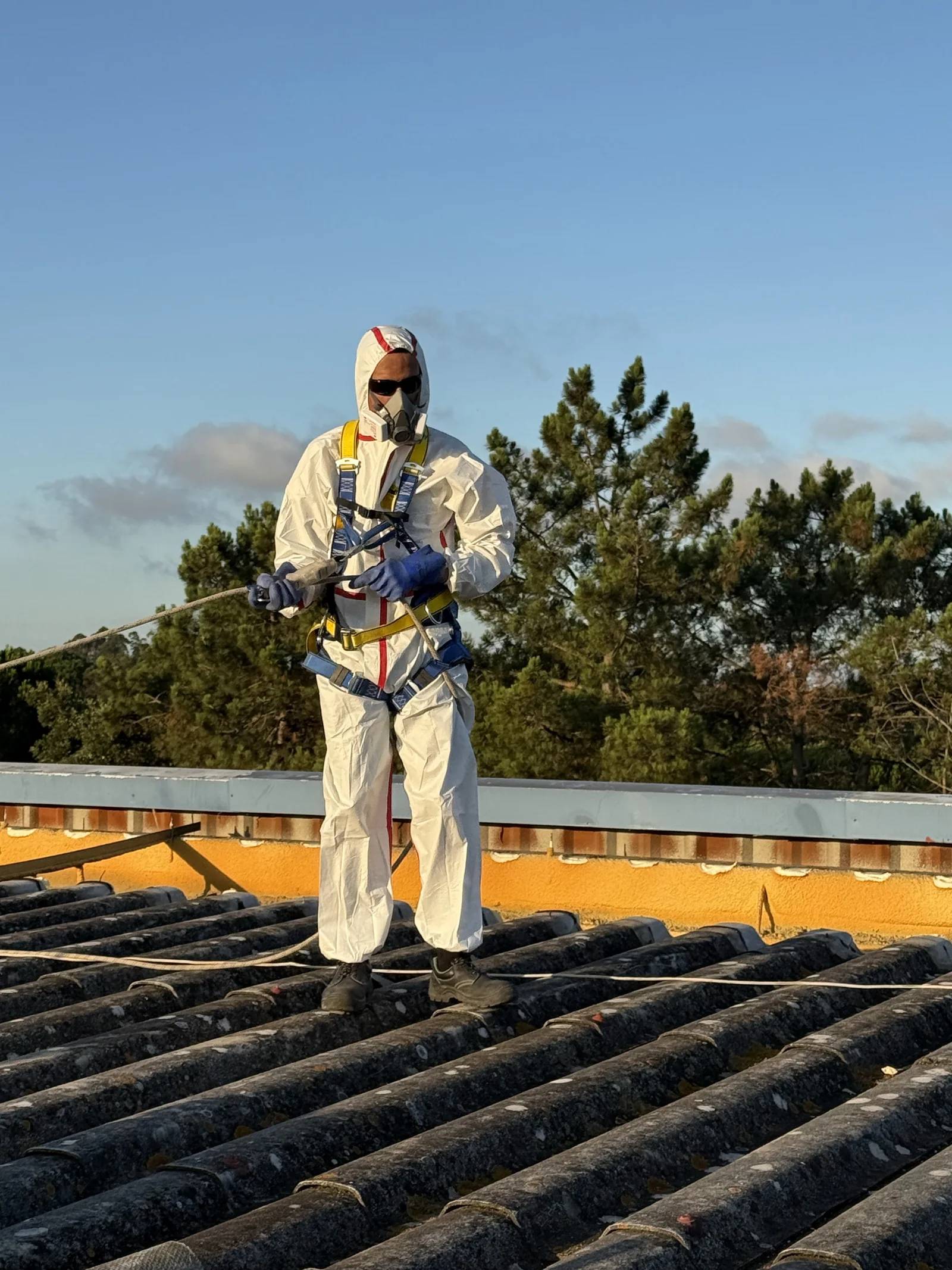Profissional numa cobertura, com fato de proteção, proteção respiratória, luvas e arnês